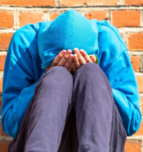 Hooded teenager holding head in hands