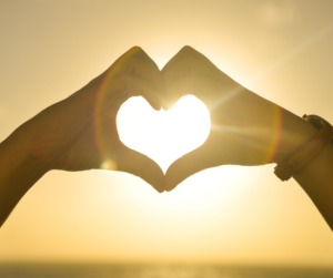 Two hands forming a heart in front of a sunset